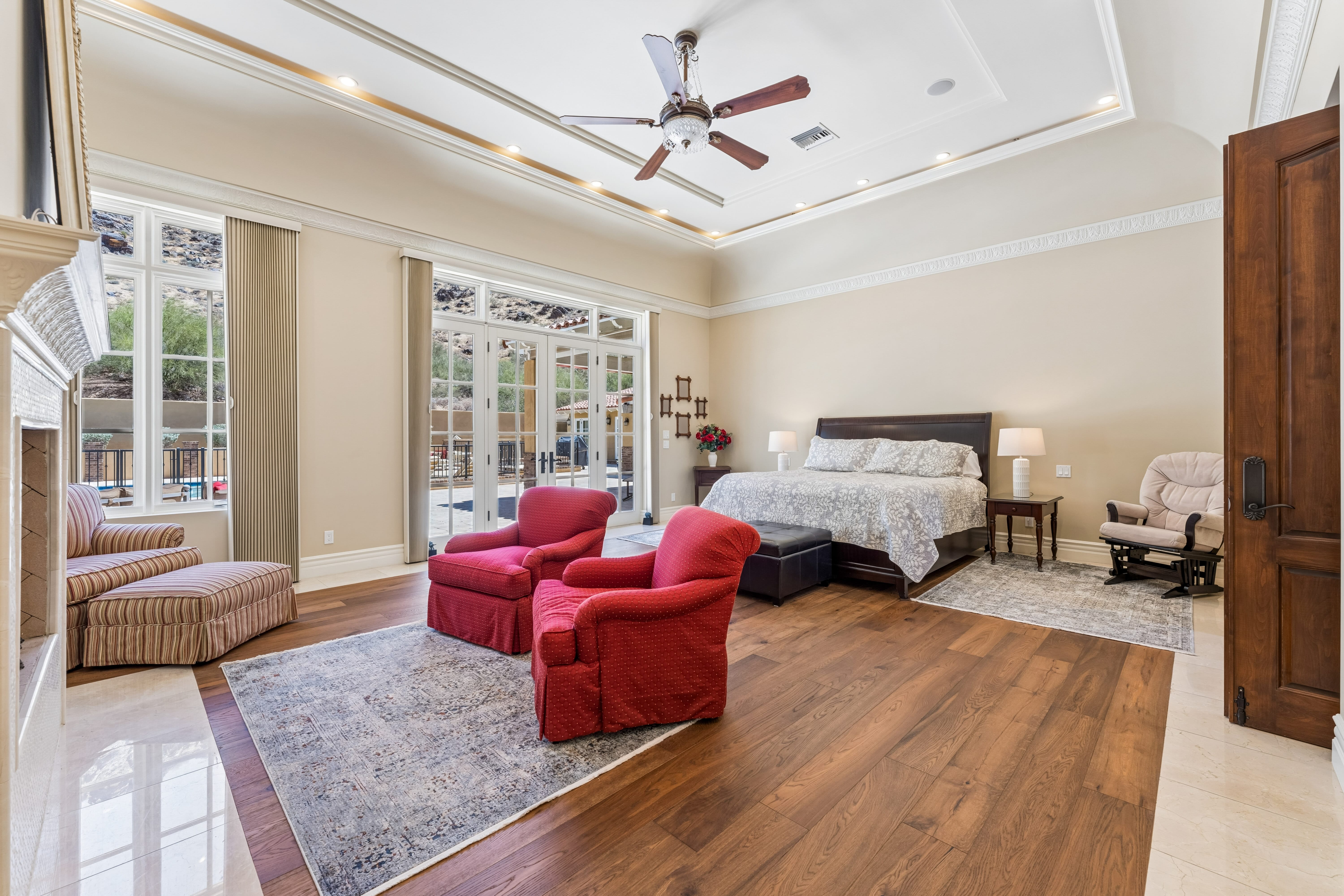 Primary bedroom with tray ceiling, fireplace, and pool terrace views