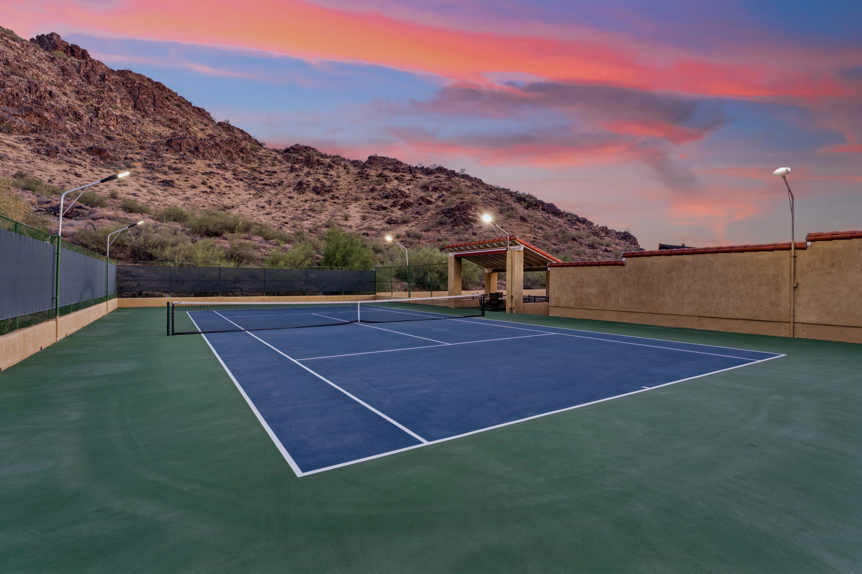 Tennis court lit at dusk under fiery sunset sky