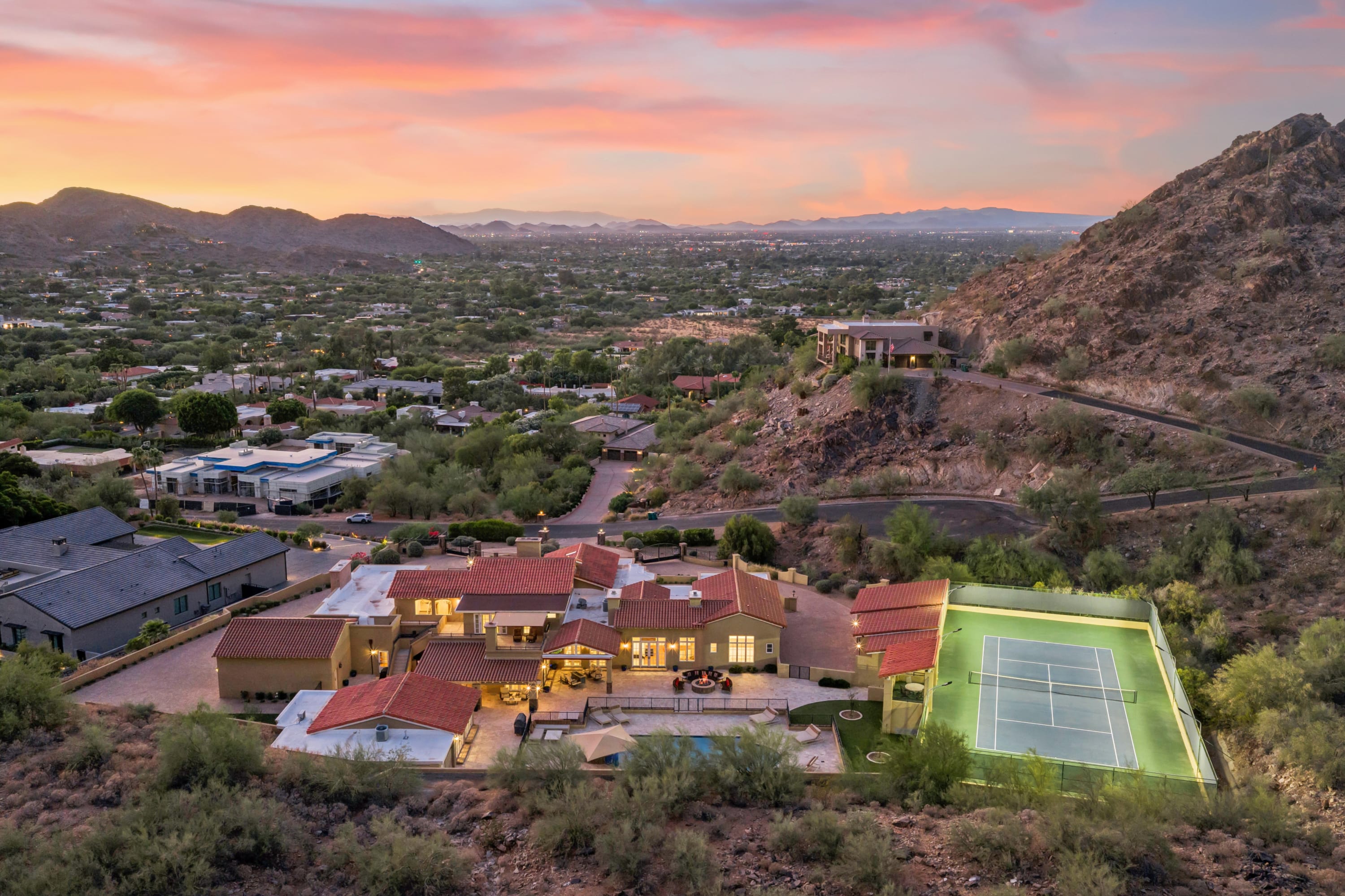 Full luxury estate at twilight with lit tennis court